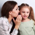 Woman Whispering To Young Girl